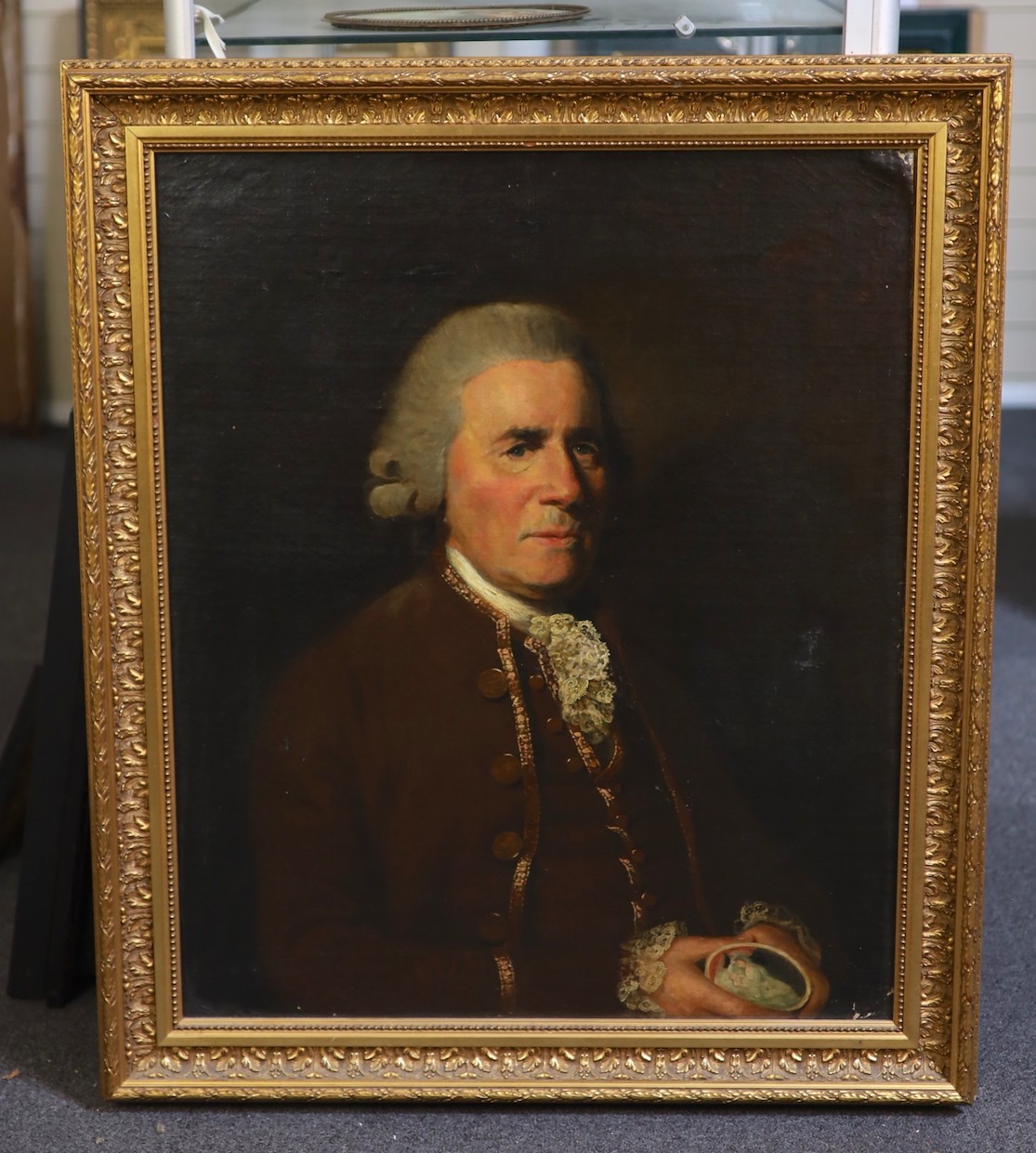 Circle of Sir Nathaniel Dance-Holland, 1st.Bt. RA (British, 1735-1811), Portrait of a gentleman, bust-length, wearing a crimson coat, white stock, and holding a miniature, oil on canvas, 74.5 x 62cm